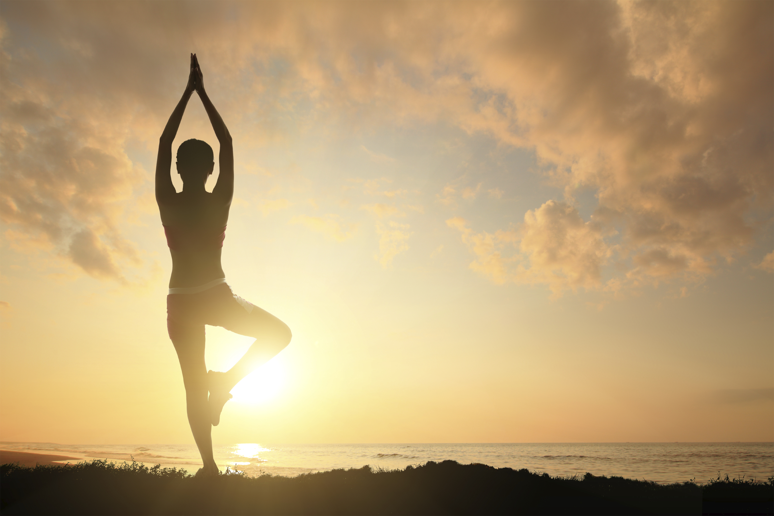 Young woman silhouette practicing yoga on the sea beach at sunset